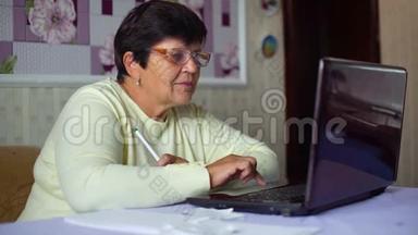 戴眼镜的老年妇女检查家里笔记本电脑的日常开支